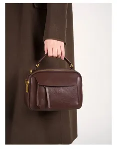 Close-up detail view of dark brown genuine leather retro handbag held by hand gracefully.