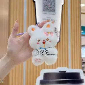 Cute plush rabbit toy keychain detail shot, soft white stuffed animal with boba tea embroidery.