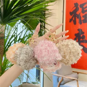 Detailed close-up shot of fluffy curly sheep plush keychains in various colors held in hand.