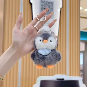 Close-up of the fluffy penguin plush keychain with soft fur, orange beak, and blue striped bib.