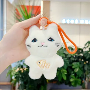 Detailed shot of cute white plush cat keychain with blue eyes and small fish embroidery.