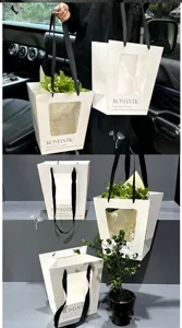 Witte papieren bloemencadeautassen met doorzichtig venster en zwarte lint handgrepen.
