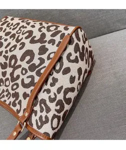 Detailansicht einer stilvollen Handtasche aus Leo-Canvas mit braunen Lederkanten und Riemen.