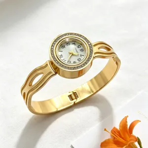 Elegante goldfarbene Spangenuhr mit kristallbesetzter Lünette und weißem Zifferblatt auf Textur.