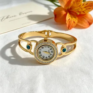 Detaillierte Ansicht einer goldenen Armreif-Uhr mit glitzernden Strasssteinen und Türkis