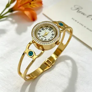 Detailansicht der goldenen Armreif-Uhr mit Strass-Lünette und blaugrünen Akzenten