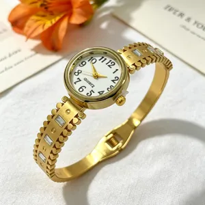 Detailansicht einer goldenen Damenarmbanduhr mit graviertem Armreif und Strasssteinen