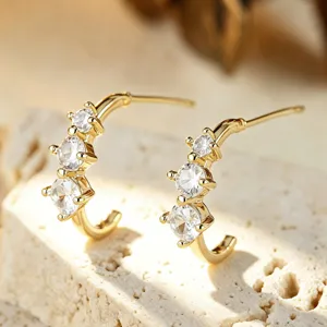 Primo piano di eleganti orecchini a lobo dorati a forma di C con pietre di zircone scintillanti.