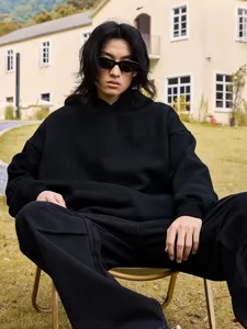 Closeup detail view of black heavyweight fleece hooded sweatshirt worn by model outdoors.