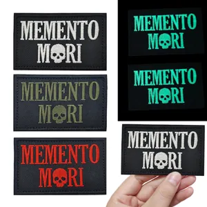 Detailed view of embroidered MEMENTO MORI patches in various colors and glow-in-the-dark styles.