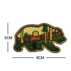 Vista detallada del parche bordado de oso con diseño de paisaje y atardecer, compacto.