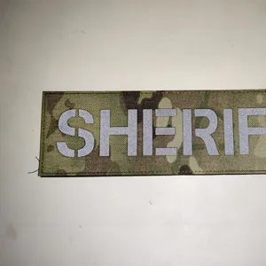 Detalle de parche reflectante para chaleco táctico con camuflaje multicam y texto.