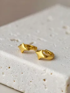 Nahaufnahme eleganter goldener vierzackiger Stern Huggie Creolen auf strukturierter Oberfläche.