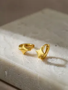 Nahaufnahme glänzender goldener vierzackiger Stern Creolen auf heller Steinoberfläche.