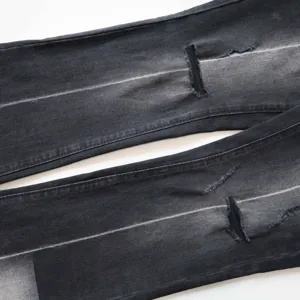 Dettaglio di jeans neri vintage a zampa con strappi e usura sulle ginocchia