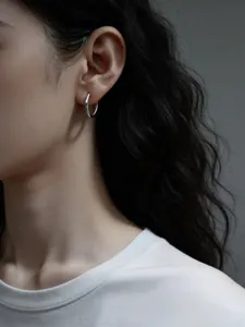 Detailaufnahme eines minimalistischen silbernen Ohrrings am Ohr im modernen Stil.