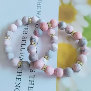 Détail de deux bracelets en perles marbrées rose et gris avec des séparateurs dorés en strass.