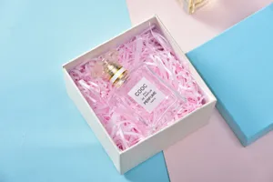 Pink raffia shredded paper gift box filler with elegant perfume bottle for festive packaging.