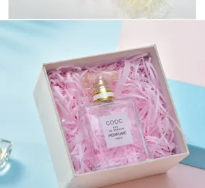 Close-up detail of perfume bottle placed in gift box with pink shredded paper filler.