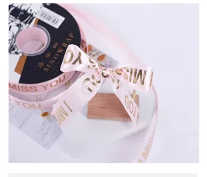 Detailed close-up of pink satin ribbon with gold stamped letters for gift packaging and crafts.