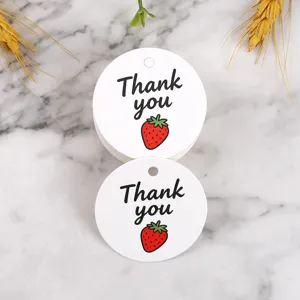 Closeup view of round white gift tags featuring cute strawberry graphic and thank you text.