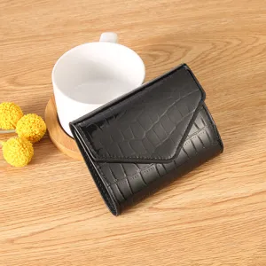 Detailed shot of a stylish black patent crocodile pattern trifold wallet on wooden table.