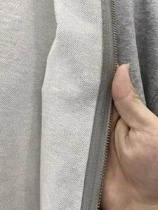 Close-up of heavy loopback fleece fabric and durable metal zipper on gray hoodie sweatshirt.