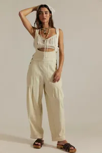 Vue détaillée du pantalon à bretelles beige et ample avec poches latérales en studio photo.
