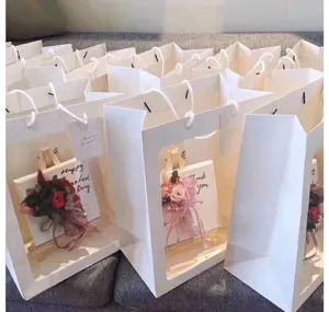 Detailopname van witte cadeautasjes met doorzichtige vensters en mini boeketjes.