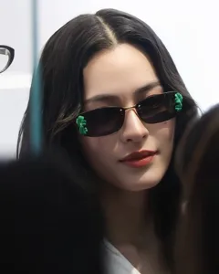 Close-up detail of trendy narrow sunglasses featuring unique green leaf decor and metal frame.