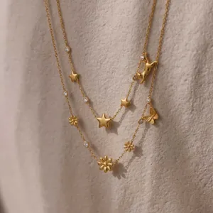 Detailopname van een dubbele gouden ketting met madeliefjes- en vlinderhangers.
