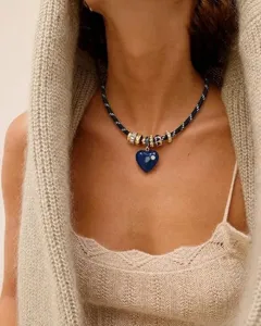 Nahaufnahme einer blauen Herz-Anhänger-Seilkette an einem Modell in beigem Stricktop