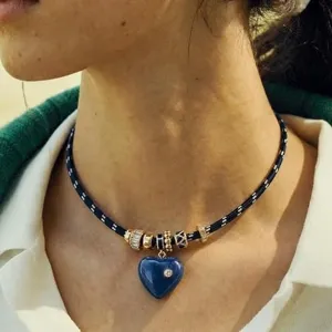 Elegante blaue Kordelkette mit Herzanhänger und Goldcharms, von einem Modell getragen.