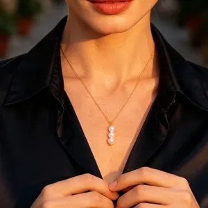 Detailed shot of a delicate gold chain necklace featuring a vertical three-pearl pendant.