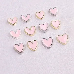 Close-up of pink enamel heart nail art charms with gold and silver metallic borders.