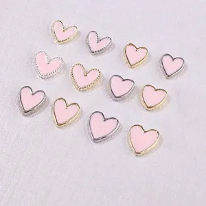 Detailed macro view of pink heart-shaped nail art charms with gold and silver metallic edges