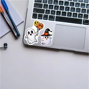 Close-up detail of cute Halloween ghost stickers displayed on a modern laptop keyboard surface.