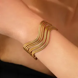 Close-up of a gold-finished multi-layer wave cuff bracelet worn on a wrist.