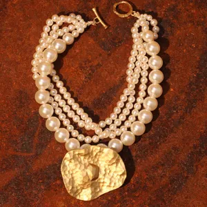 Elegante collar de perlas de varias capas con un gran colgante de metal dorado martillado.