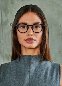Primer plano detallado de gafas ópticas clásicas de montura negra usadas contra pared gris.