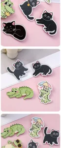 Close up of cute black cat and green crocodile acrylic pins, smooth surface, detailed.