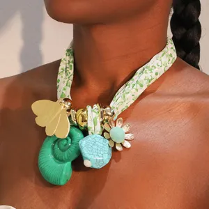 Primer plano de un collar de bufanda bohemio estampado verde con dijes de mariposa y caracola