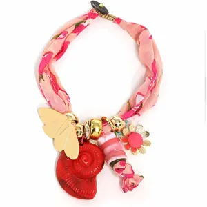 Detalle de collar de seda bohemio con mariposa dorada y colgante de caracol rojo