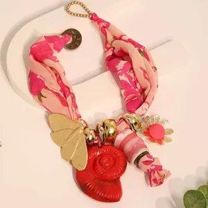 Primer plano de collar de pañuelo bohemio con mariposa de metal y concha roja.