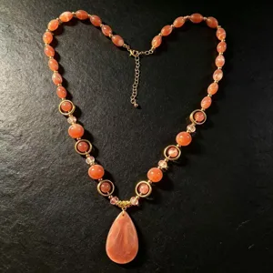 Close-up of a handmade resin beaded necklace with orange teardrop pendant