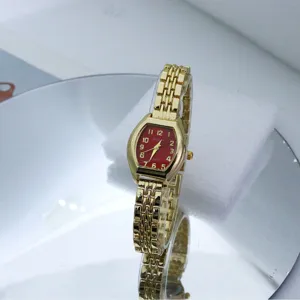 Close-up view of the luxury gold tone quartz watch with red tonneau dial and metal bracelet strap.