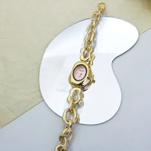Detailansicht der goldenen unregelmässigen Kettenuhr mit pinkem Zifferblatt und Design Detail.