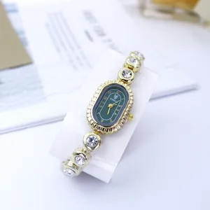 Nahaufnahme der goldenen Damen-Armbanduhr mit ovalem grünen Zifferblatt und Strasssteinen.