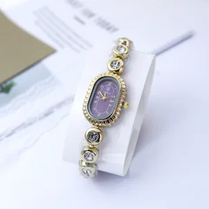 Detailaufnahme einer goldenen Damen-Armbanduhr im Vintage-Stil, lila ovales Zifferblatt mit Strass.