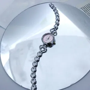 Detailaufnahme einer Herzgliederarmbanduhr mit rosa Pony Zifferblatt und Metallketten.